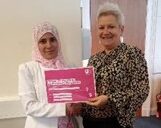 a muslim woman wearing a pink headscarf and a white woman wearing a leopard print shirt are smiling and holding up a (pink) certificate of completion